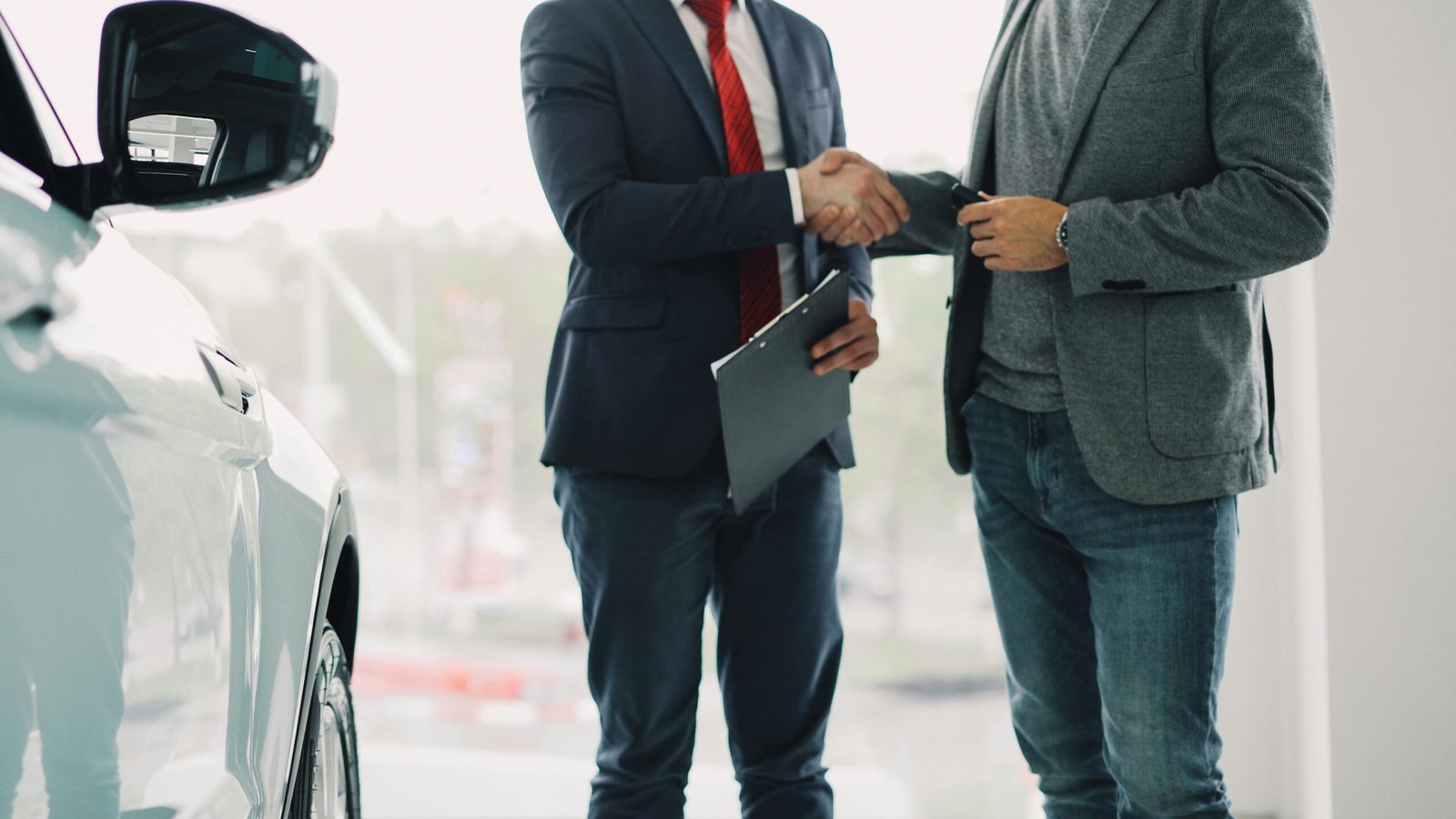 Two men shake hands in a car dealership, sealing a business deal.