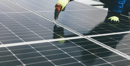 A technician uses a power tool to install solar panels, showcasing renewable energy efforts.
